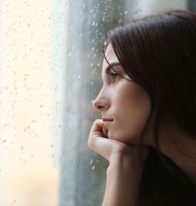 Woman feeling sad looking out a window wet from rain