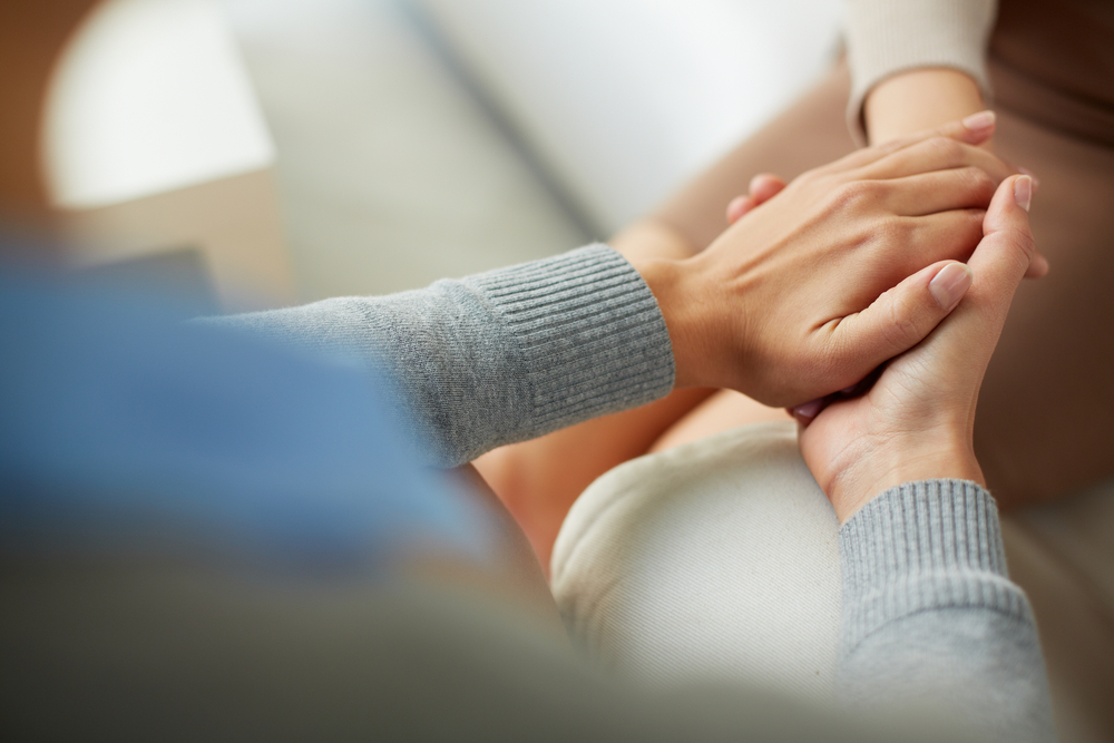 Close up of psychiatrist with patient offering support by holding hands.