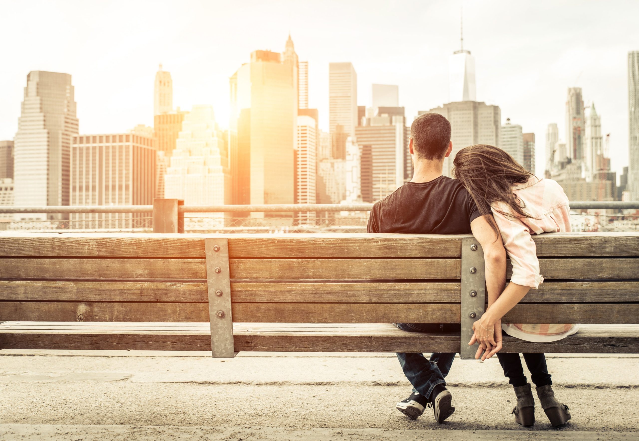 Couple sitting on a park bench enjoying a view of Manhatten and holding hands