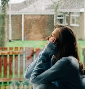 sad woman sitting on a windowsill with a reflection on a window